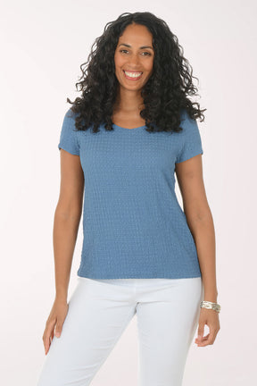 Woman wearing a blue textured top and white pants on a white background