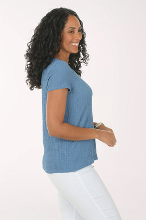 Woman wearing a blue textured top and white pants on a white background