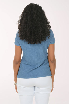 Woman wearing a blue textured top and white pants on a white background