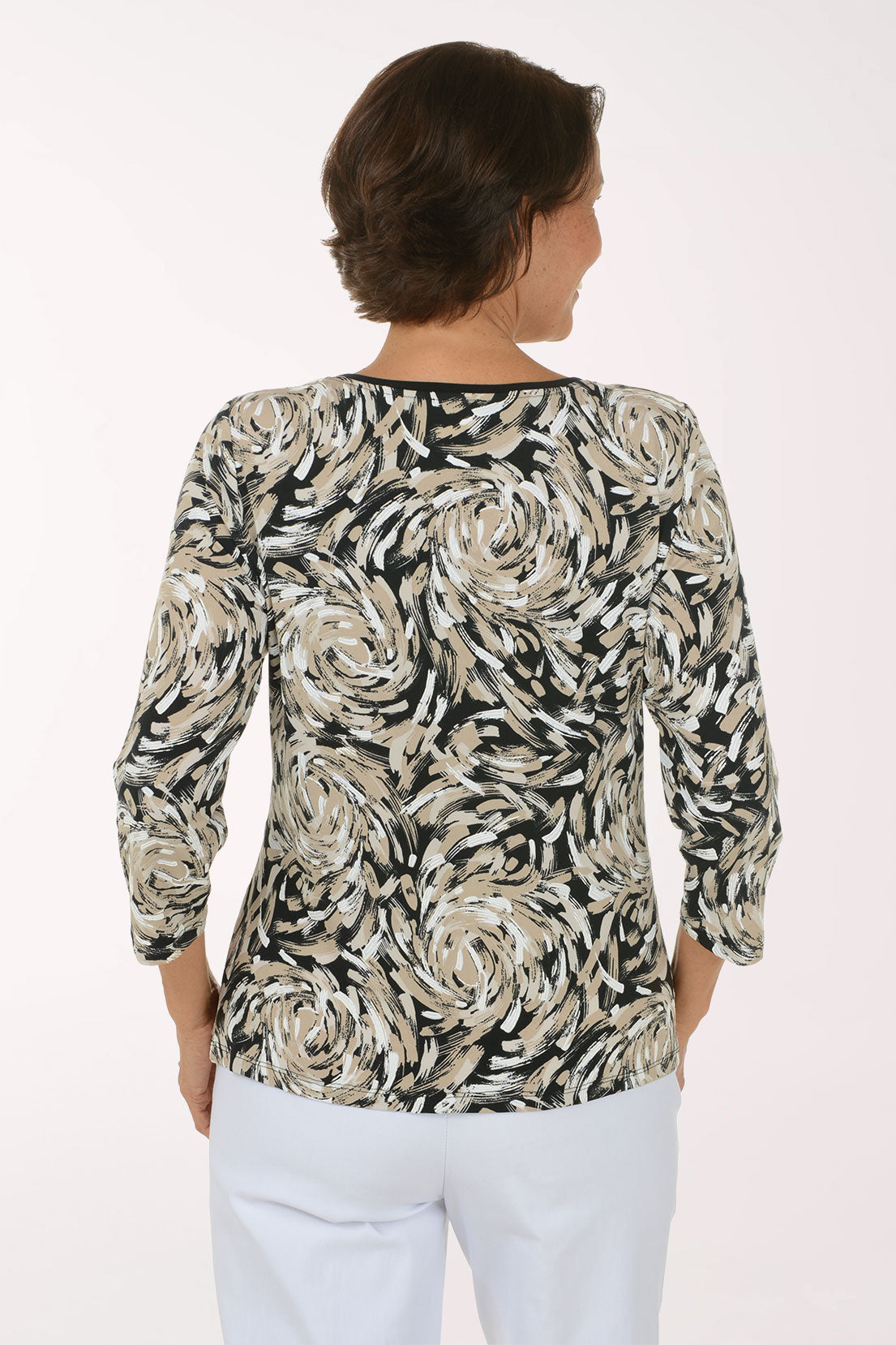 A woman modeling a three-quarter sleeve top with a black, white, and beige floral swirl pattern and a side tie, paired with white pants against a plain white background.