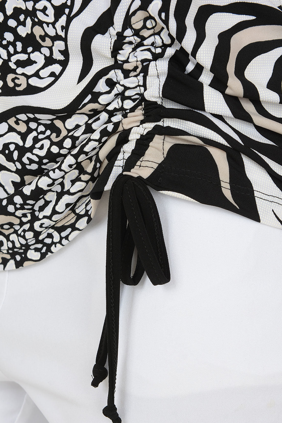 A woman modeling a black and white zebra print top with three-quarter sleeves and a side tie, paired with white pants, against a plain light background.
