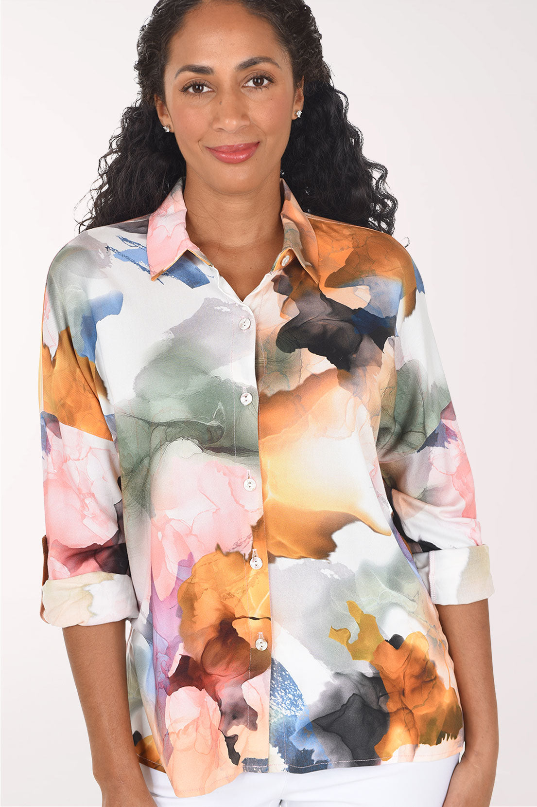 A woman wearing a long-sleeve button-up shirt with a colorful abstract watercolor floral print, set against a plain light background.