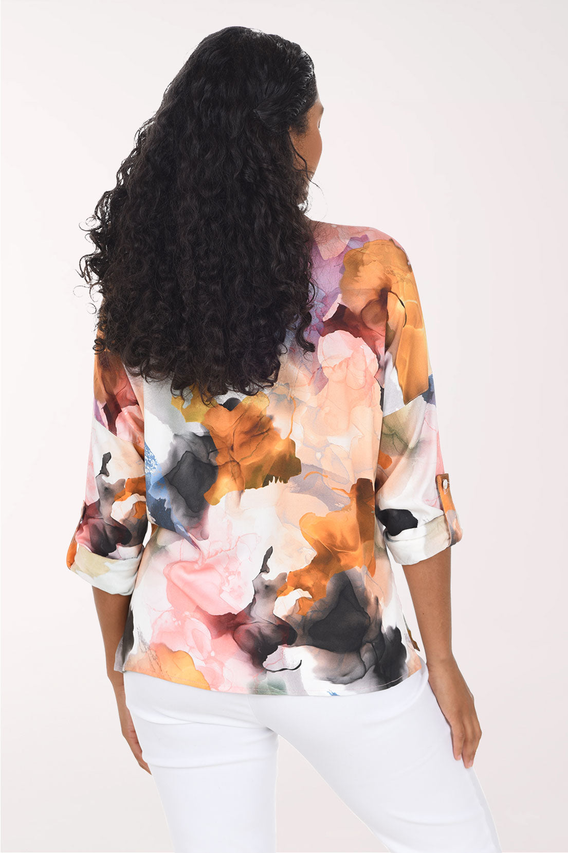 A woman wearing a long-sleeve button-up shirt with a colorful abstract watercolor floral print, set against a plain light background.