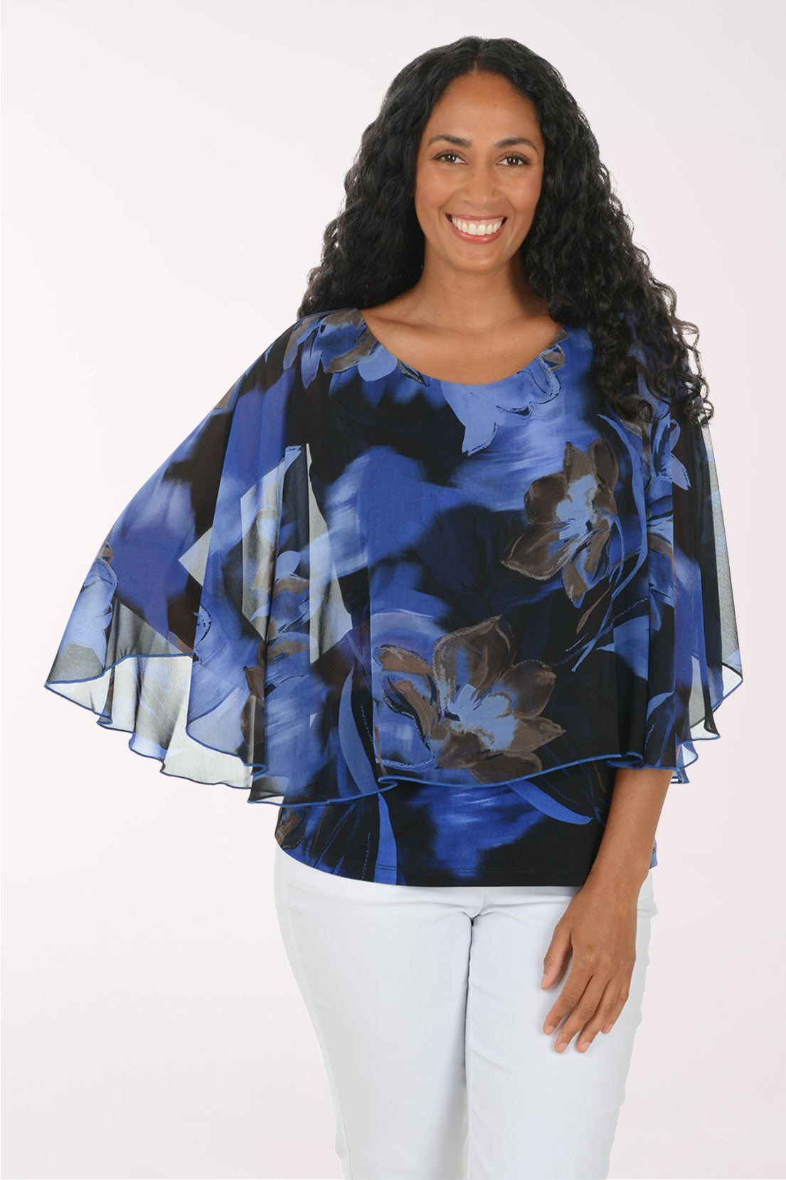 A woman wearing a blue and black abstract floral print blouse with wide flutter sleeves, paired with white pants, photographed against a plain light background.