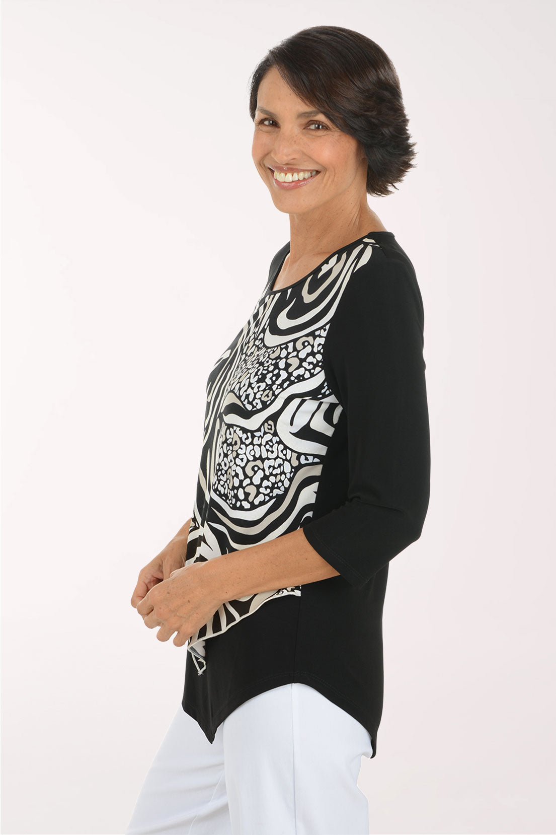 A woman modeling a black three-quarter sleeve top with a bold black and white zebra and leopard print pattern on the front panel, paired with white pants, against a plain white studio background.
