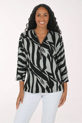 A woman modeling a black and gray abstract patterned top with a half-zip neckline, paired with white pants, against a plain light background.