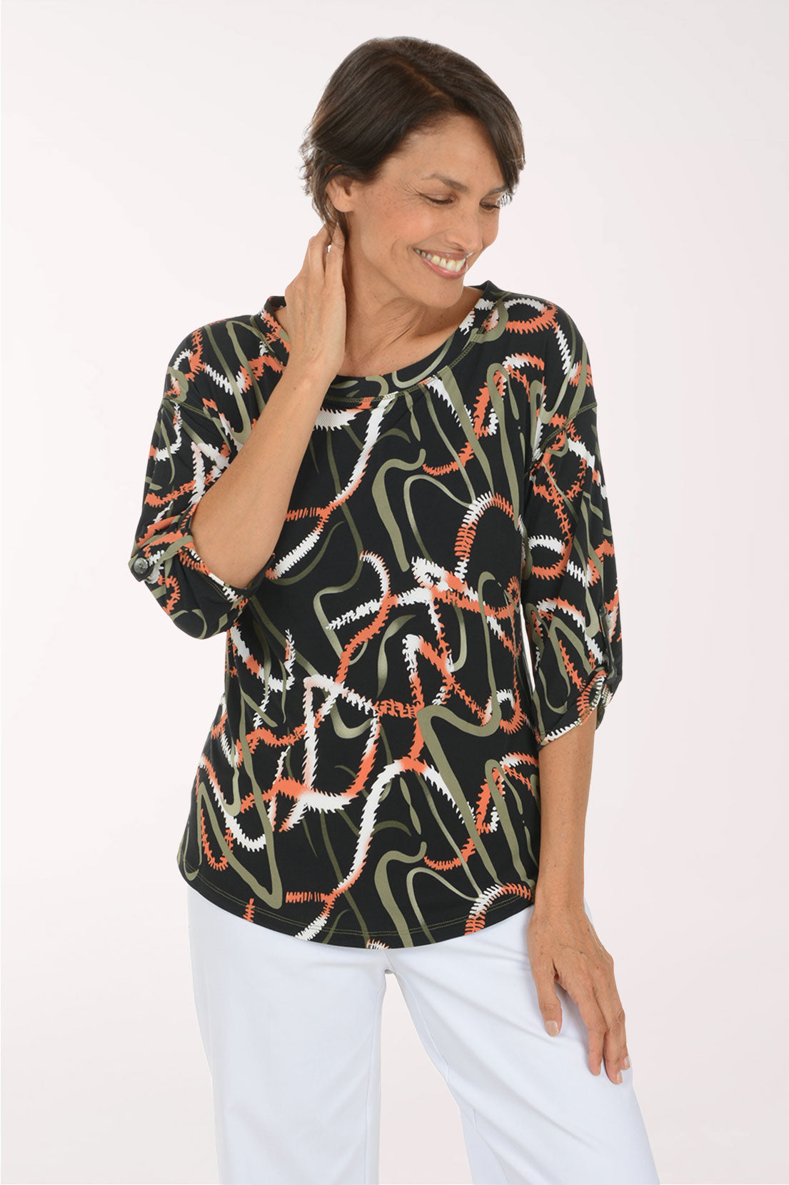 A smiling woman wearing a black three-quarter sleeve top with an abstract wavy pattern in white, orange, and olive green, paired with white pants, against a plain white studio background.
