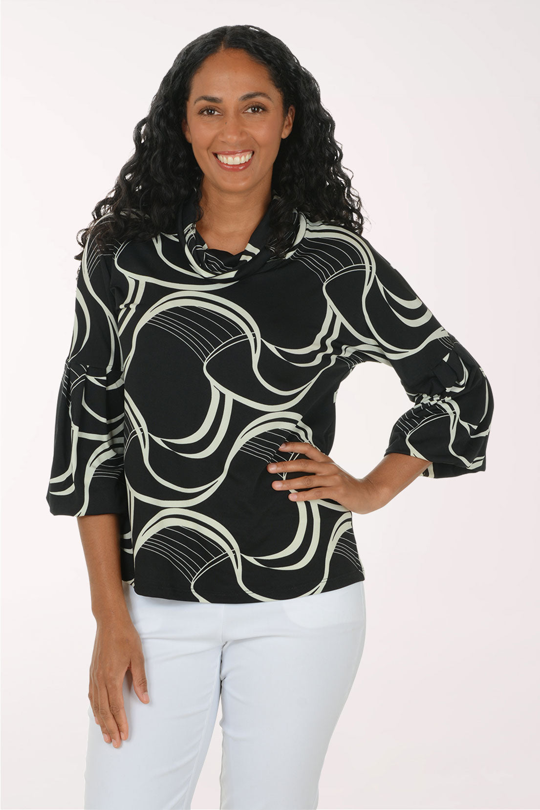 A woman modeling a black three-quarter sleeve blouse with a white abstract wavy pattern, paired with white pants, against a plain white studio background.