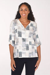 A woman modeling a white three-quarter sleeve top with a gray and blue abstract block pattern, paired with black pants, against a plain white studio background.