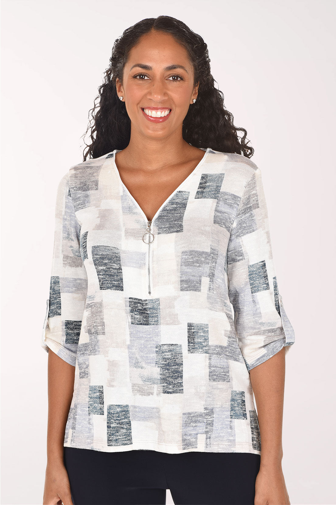 A woman modeling a white three-quarter sleeve top with a gray and blue abstract block pattern, paired with black pants, against a plain white studio background.
