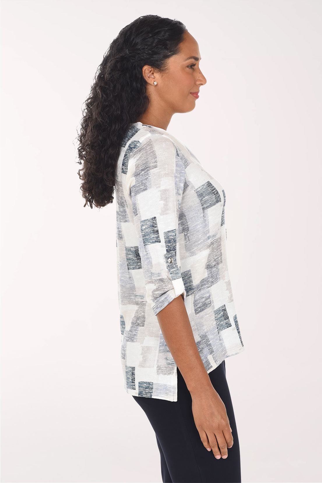 A woman modeling a white three-quarter sleeve top with a gray and blue abstract block pattern, paired with black pants, against a plain white studio background.