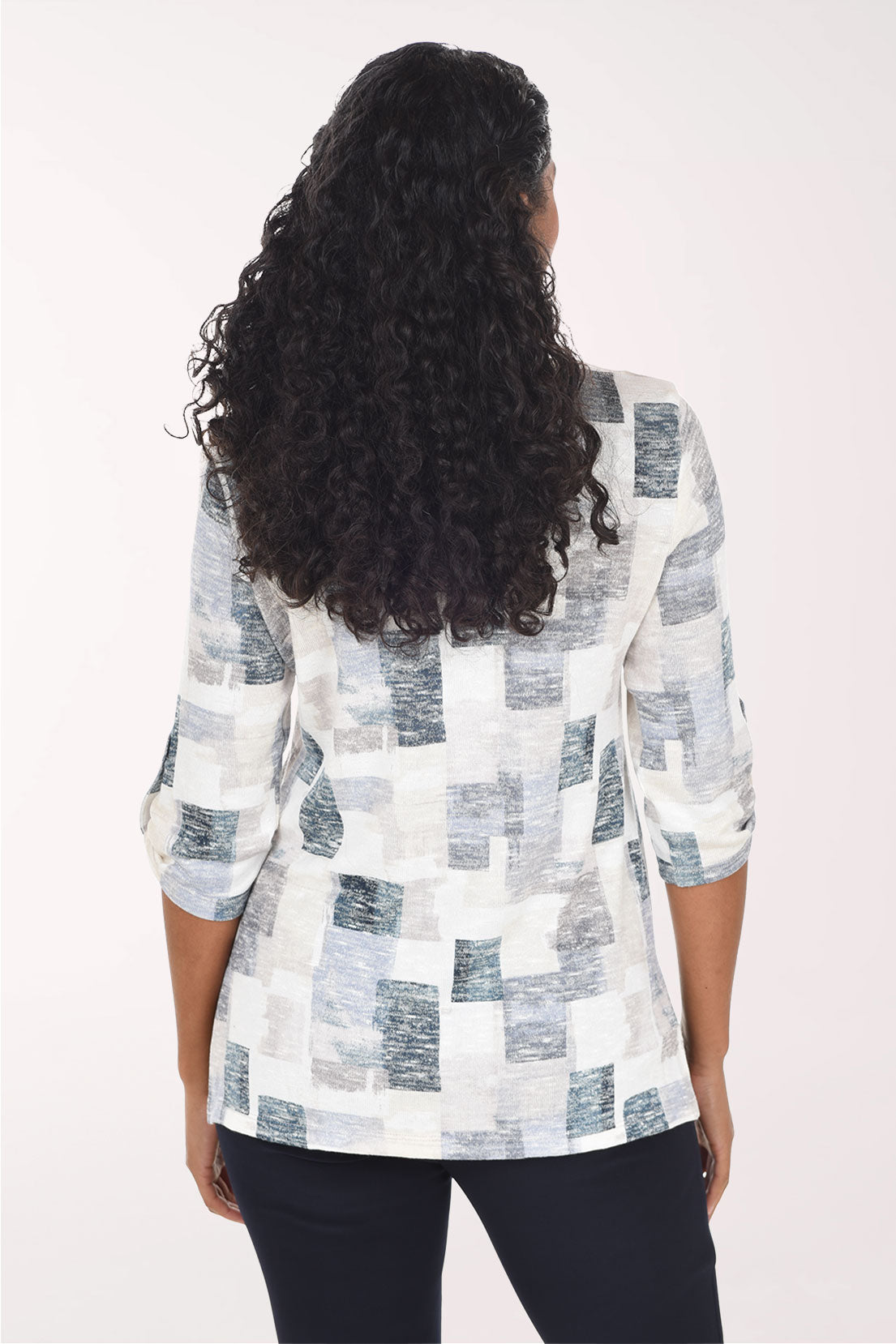 A woman modeling a white three-quarter sleeve top with a gray and blue abstract block pattern, paired with black pants, against a plain white studio background.