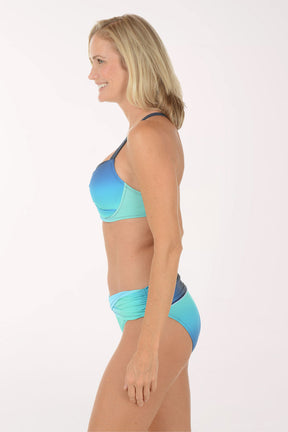 Woman wearing a blue and green bikini on a white background. Side shot.