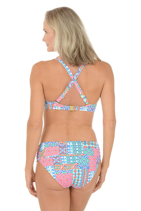 A woman wearing a multi-colored bikini top with a twist front detail. Back shot.
