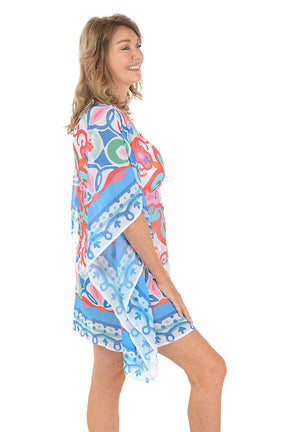 A woman wearing a multi-colored caftan over a white swimsuit. Side shot.