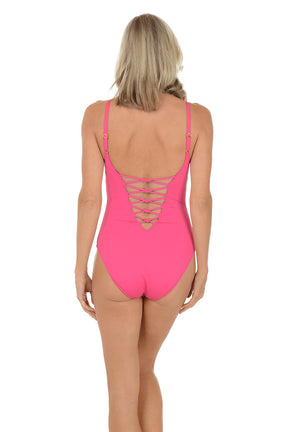 A woman wearing a pink one piece swimsuit with a lace detail on the bust. Back shot.