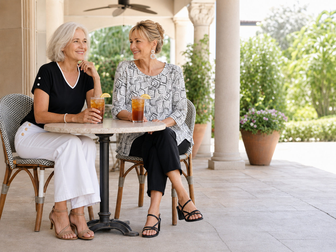 Two women sitting at a cafe enjoying iced tea wearing black and white outfits