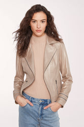A woman modeling a light beige faux-leather moto jacket over a ribbed beige turtleneck sweater and blue jeans, photographed against a clean white studio background.