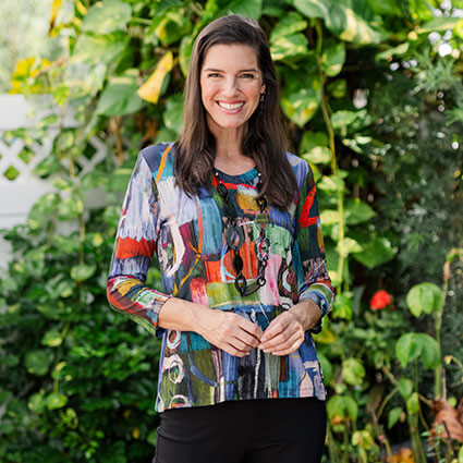 Woman wearing a colorful patterned top standing in front of green foliage