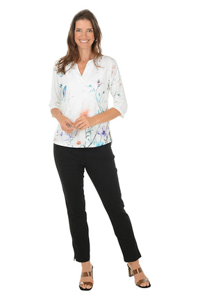 Woman wearing a white blouse with floral patterns and black pants on a white background