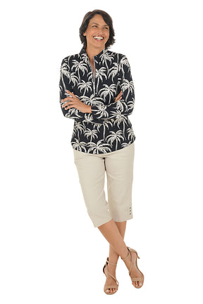 Woman wearing a black and white palm tree patterned shirt with beige pants on a white background