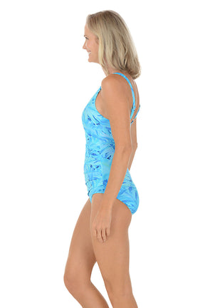 A woman wearing a blue one piece swimsuit with a leaf pattern. Side shot.
