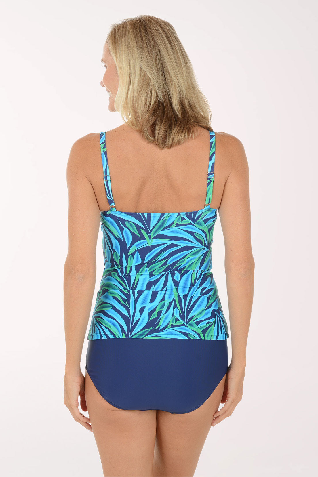 Woman wearing a blue and green leaf-patterned tankini top with navy high-waisted bottoms on a white background. Back shot.