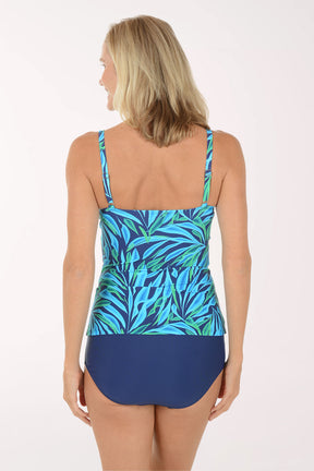 Woman wearing a blue and green leaf-patterned tankini top with navy high-waisted bottoms on a white background. Back shot.