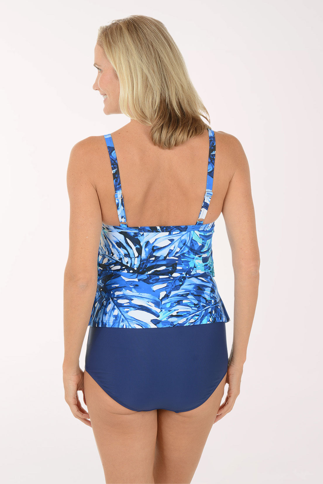 Woman wearing a blue floral tankini top and navy high-waisted bottoms on a white background. Back shot.