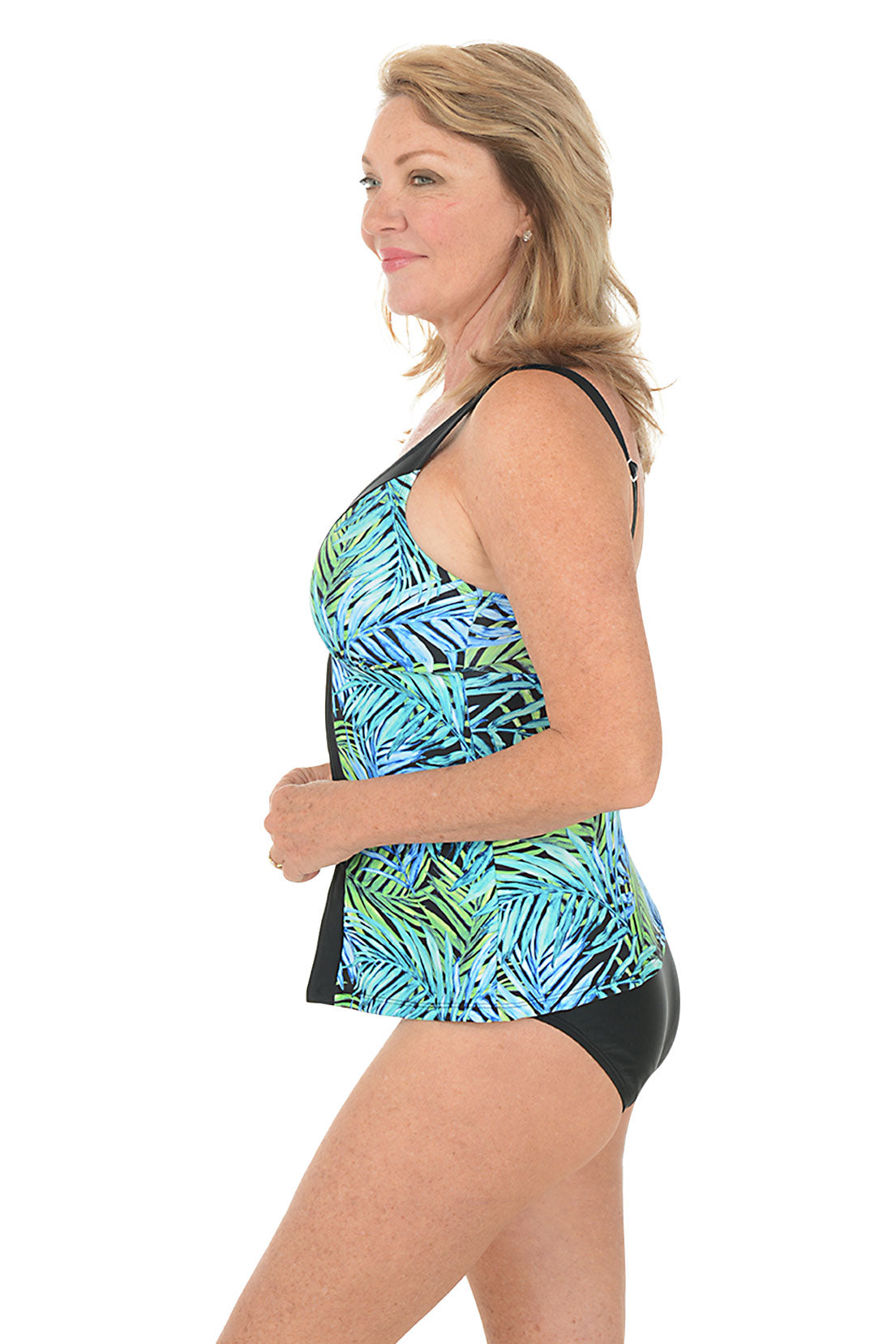 Woman wearing a tropical print tank top and black swimsuit bottom on a white background. Side shot.