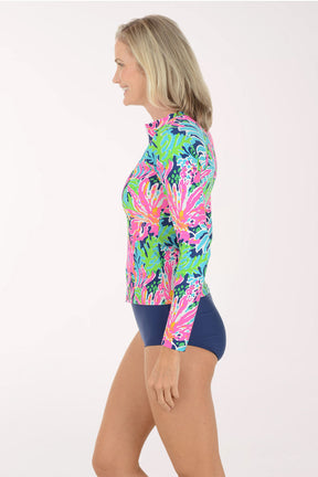 Woman wearing a colorful long-sleeve rash guard with a white background. Side shot.