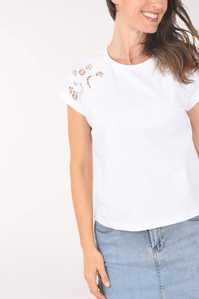 Woman wearing a white top with floral embellishments and a denim skirt on a white background