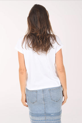 Woman wearing a white top with floral embellishments and a denim skirt on a white background