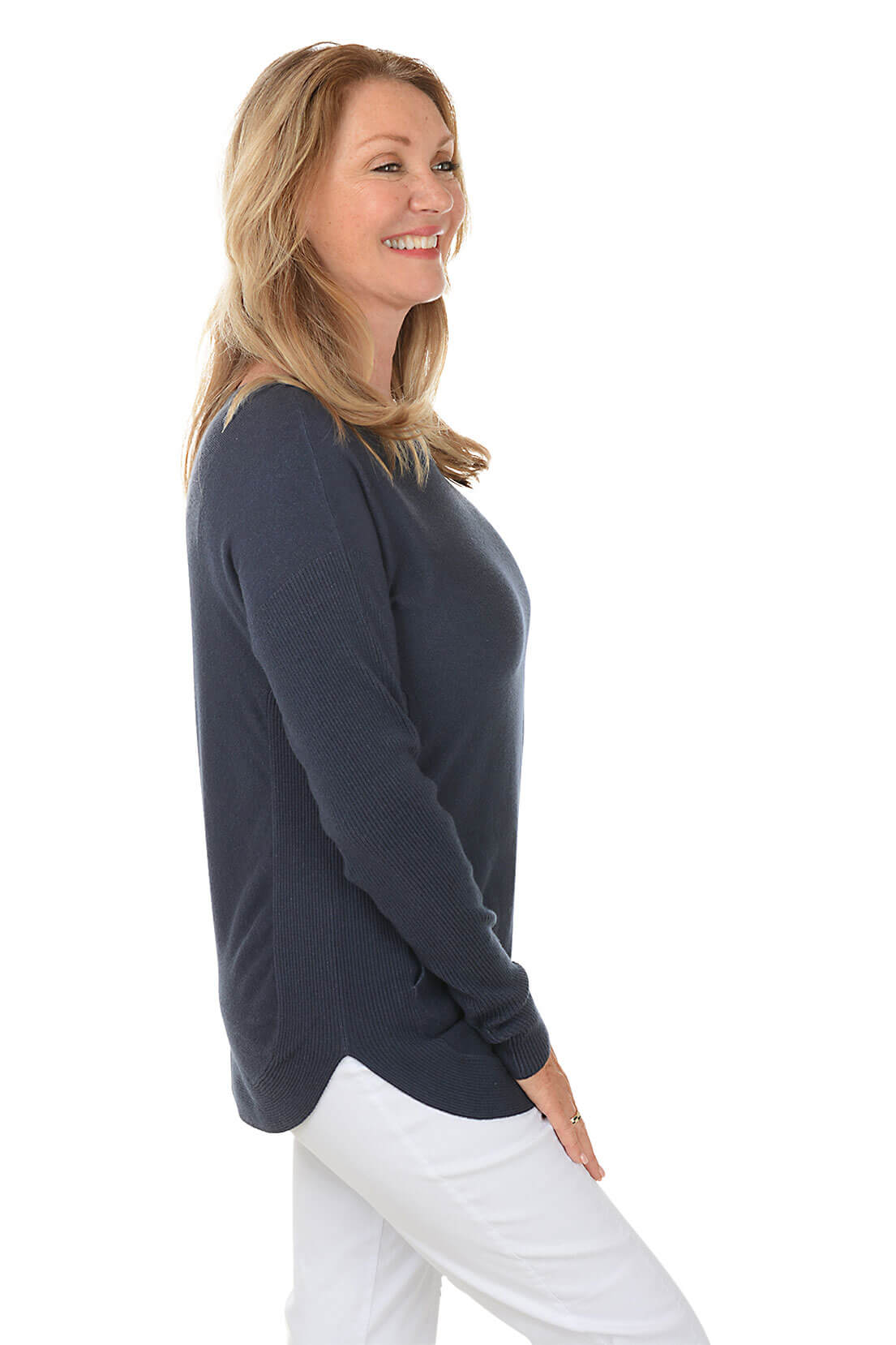 Woman wearing a navy blue sweater and white pants on a white background. Side shot.