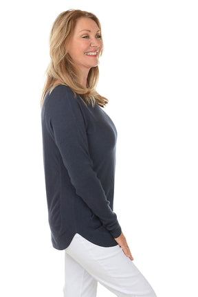 Woman wearing a navy blue sweater and white pants on a white background. Side shot.