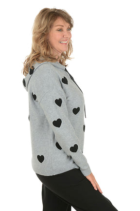Woman wearing a gray hoodie with black heart patterns on a white background. Side shot.