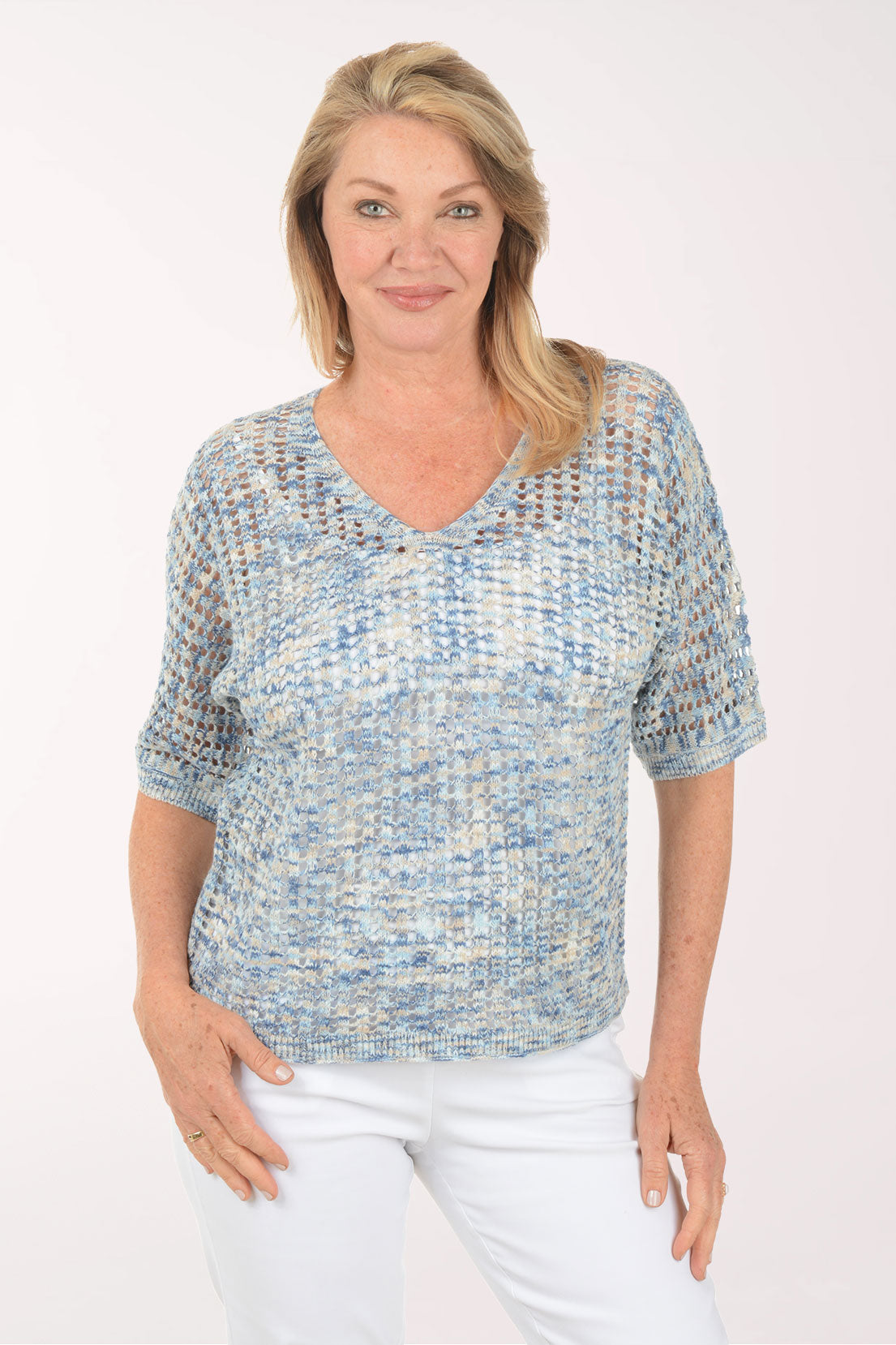 Woman wearing a textured blue top and white pants on a white background