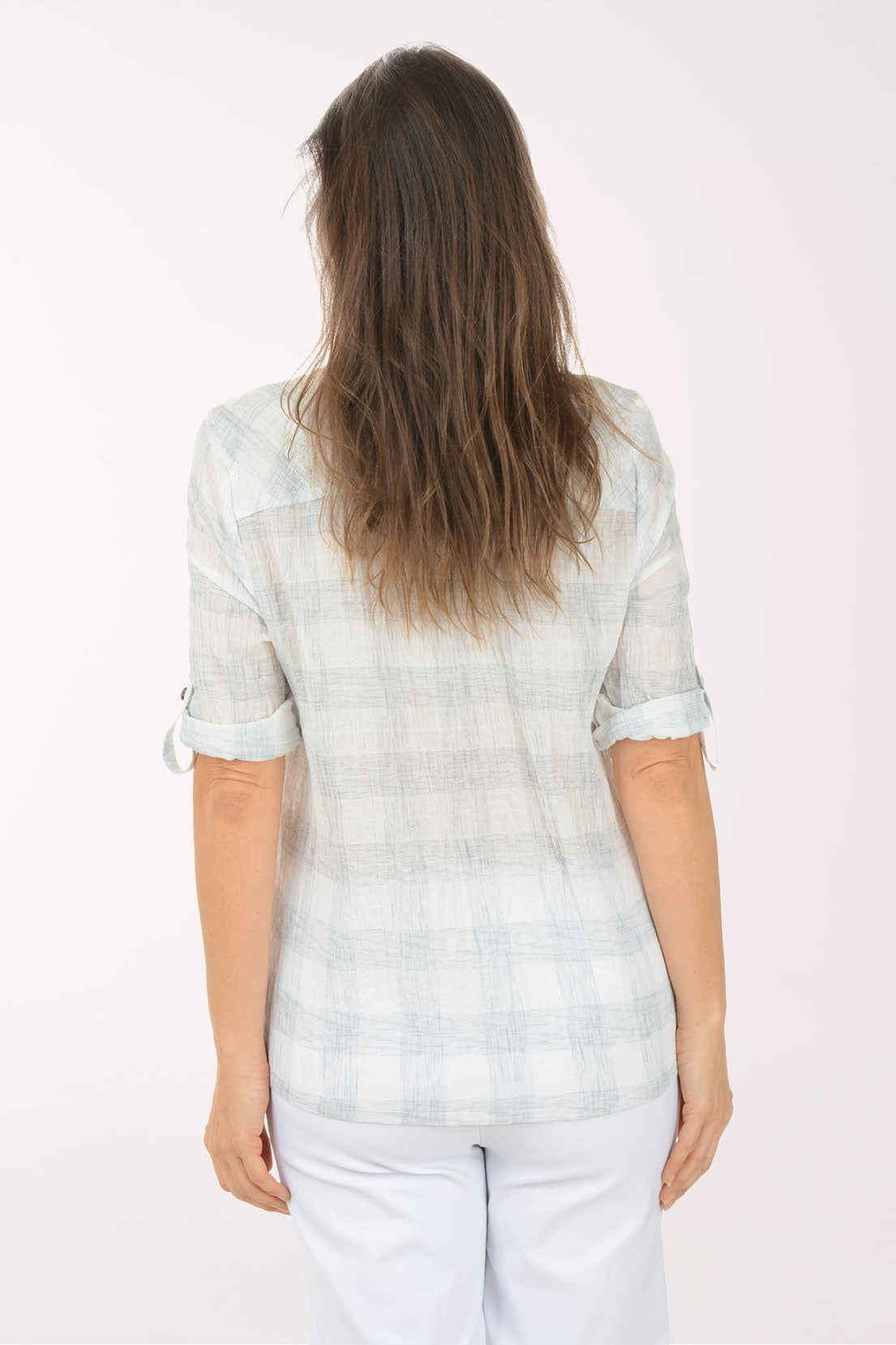 Woman wearing a light-colored blouse with rolled-up sleeves on a white background