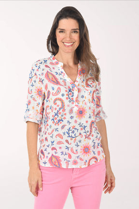 Woman wearing a colorful patterned blouse and pink pants on a white background