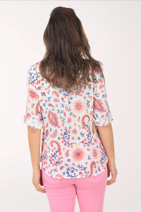 Woman wearing a colorful patterned blouse and pink pants on a white background