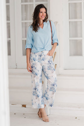 Woman wearing a light blue shirt and floral pants standing on a white staircase.