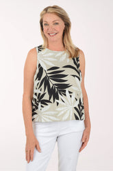 Woman wearing a sleeveless top with leaf pattern and white pants on a plain background