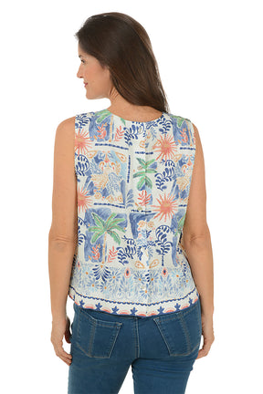 Woman wearing a sleeveless floral top with palm trees and blue jeans on a white background