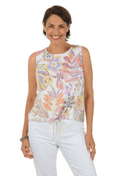 Woman wearing a sleeveless floral top and white pants on a white background