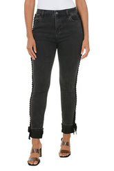 Person wearing black jeans with ruffled edges on a white background.