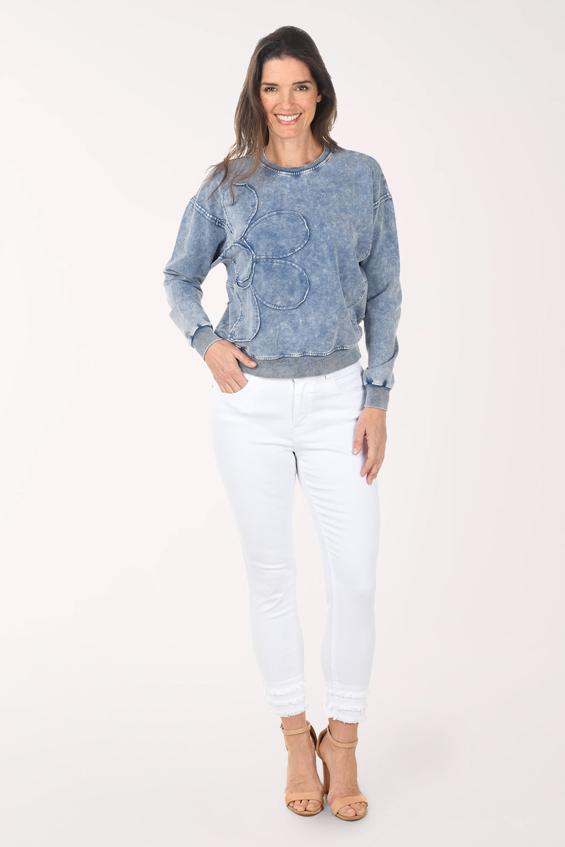 Woman wearing a blue denim sweatshirt and white pants on a white background