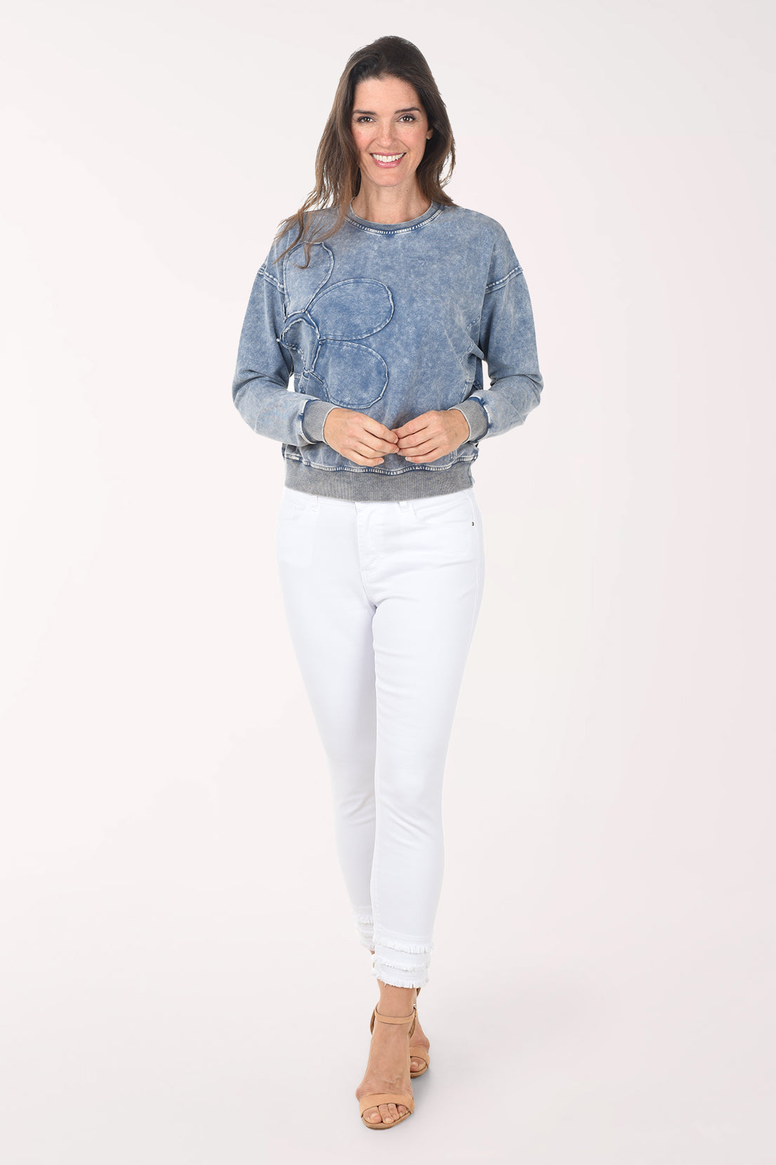 Woman wearing a blue denim sweatshirt and white pants on a white background