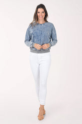 Woman wearing a blue denim sweatshirt and white pants on a white background