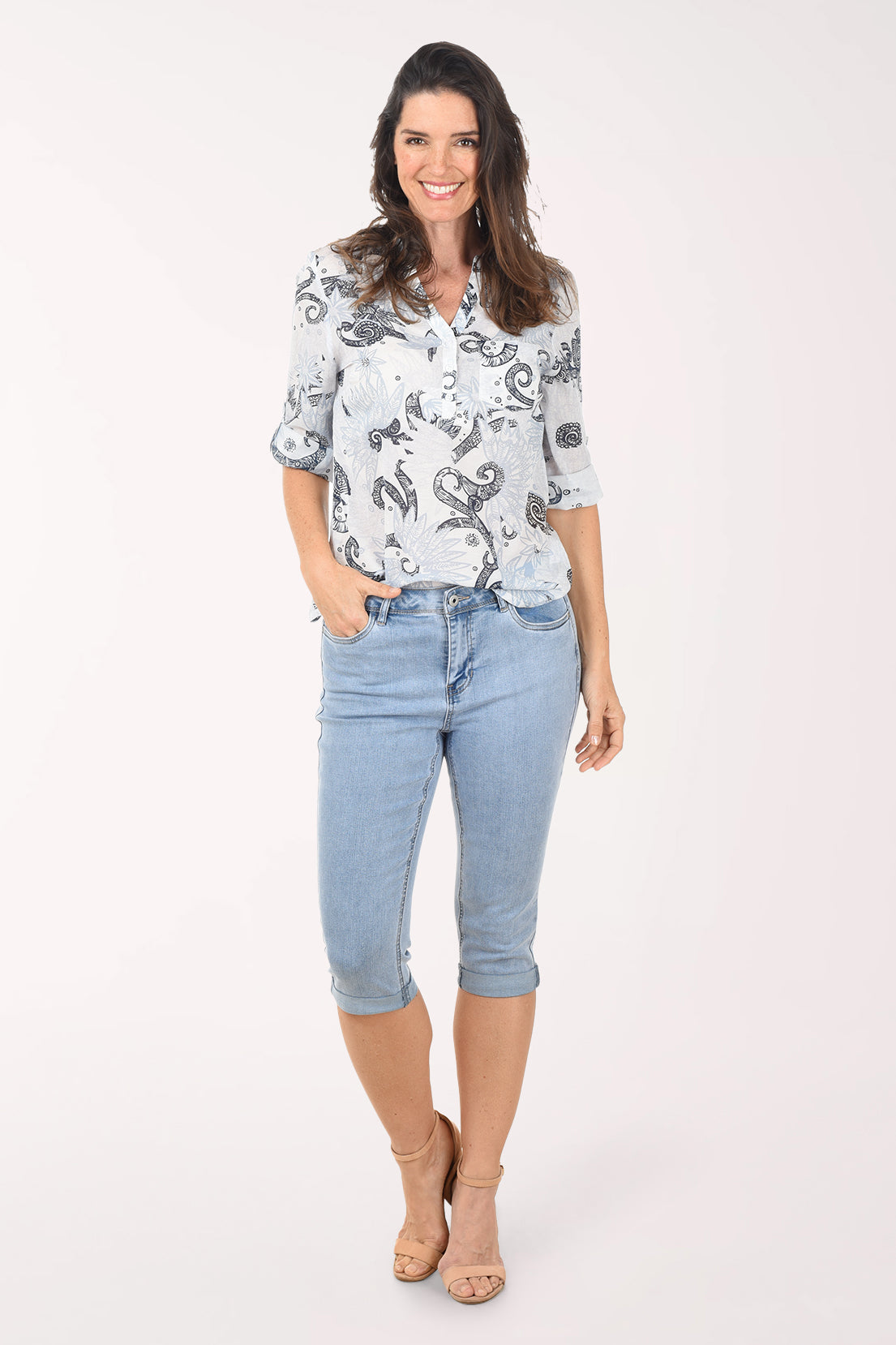 Woman wearing a patterned blouse and light blue jeans on a white background