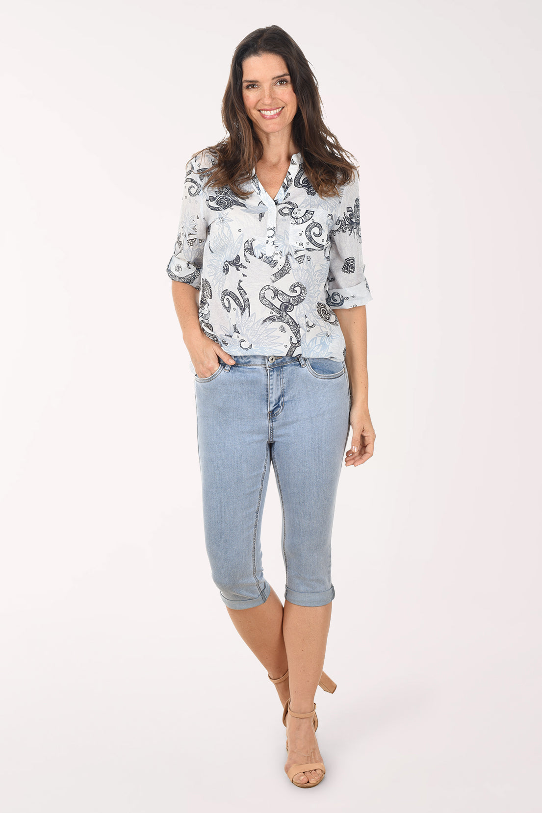 Woman wearing a patterned shirt and light blue jeans on a white background